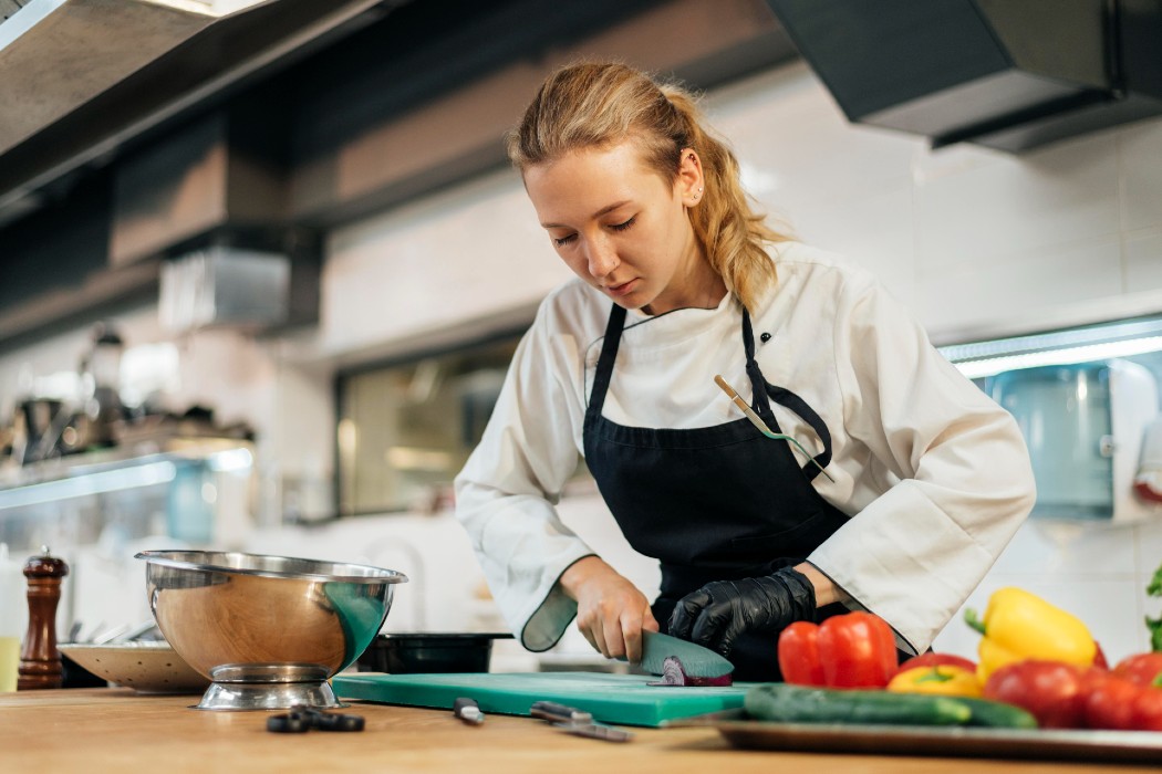 Une femme cuisinier émince des légumes sur une planche à découper