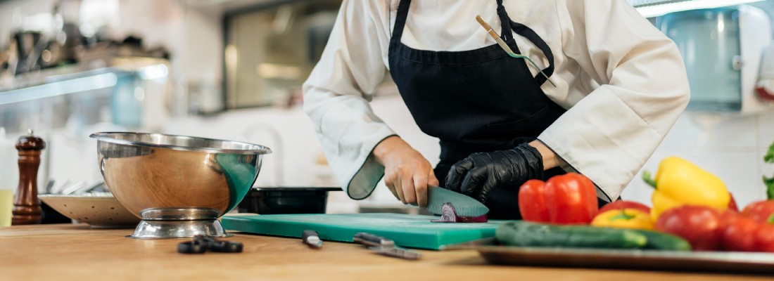 Une femme cuisinier émince des légumes sur une planche à découper